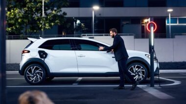 Véhicule blanc branché à une borne de recharge par un homme